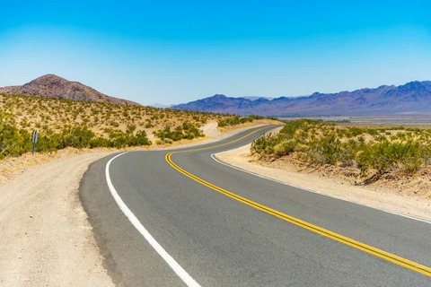 Bochtige plattelandsweg in de Mojave-woestijn, met bergen op de achtergrond.