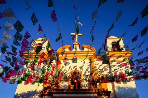 Een kleurrijke kerk in koloniale stijl, te zien te midden van kleurrijke versieringen, met de blauwe lucht op de achtergrond, in San Cristóbal de las Casas, Mexico