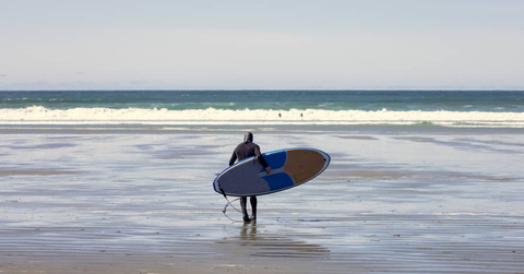 Surfer loopt in de zee bij Tofino, Vancouver Island