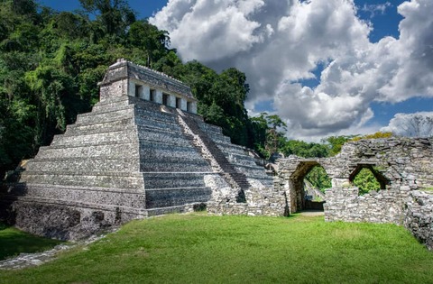 Oude Maya-tempelruïnes in Palenque, Mexico, onder een indrukwekkende bewolkte hemel, omgeven door weelderig groen.