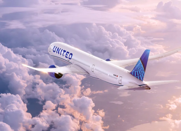 Vliegtuig van United Airlines in blauwe livrei vliegt schuin omhoog door een roze getinte wolkenlucht