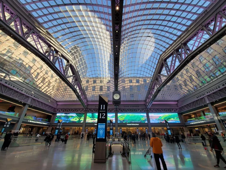 Grote hal met een gebogen glazen dak en reizigers op de vloer van de Moynihan Train Hall in New York