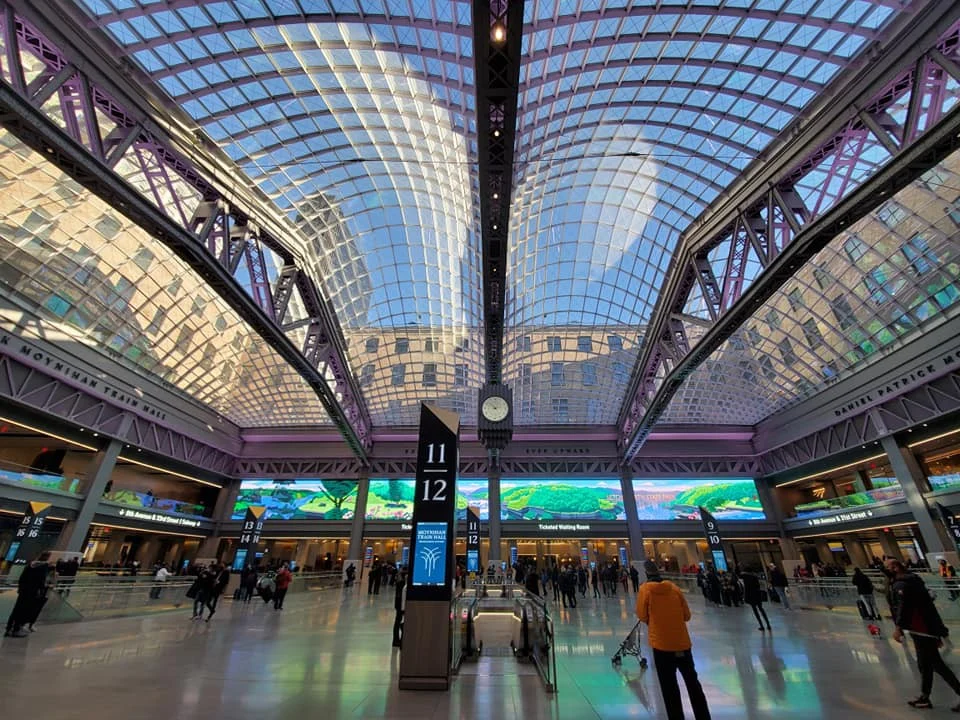 Grote hal met een gebogen glazen dak en reizigers op de vloer van de Moynihan Train Hall in New York