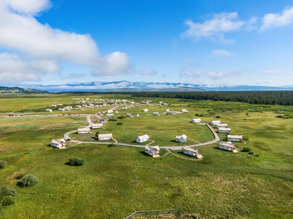 Luchtfoto van een cirkelvormig opgesteld glampingkamp met witte tenten in open grasland met bergen op de achtergrond