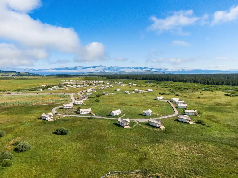 Luchtfoto van een cirkelvormig opgesteld glampingkamp met witte tenten in open grasland met bergen op de achtergrond