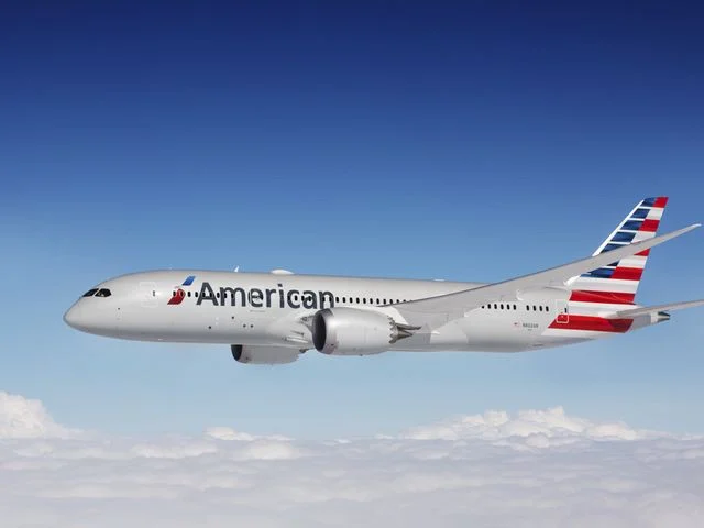 Vliegtuig van American Airlines schuin in de lucht boven een dik wolkendek met een strak blauwe lucht erboven