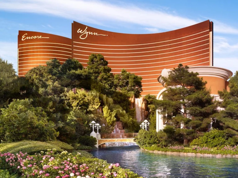 Goudkleurige gebogen torens van de hotels Wynn en Encore in Las Vegas omringd door groen en een waterval met bruggetje