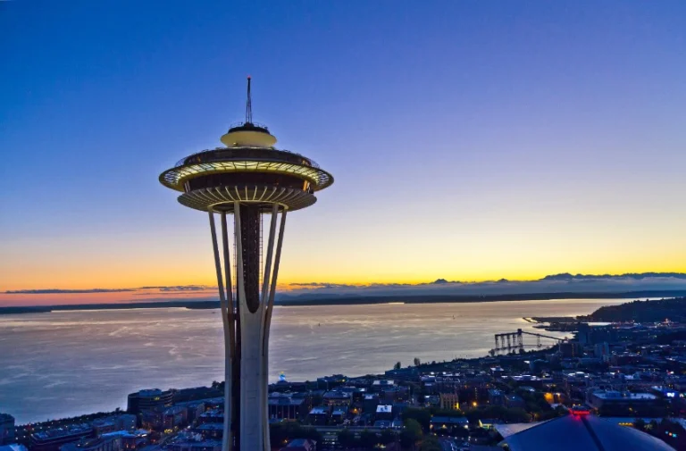 De Space Needle torent uit boven de skyline van Seattle bij zonsondergang met de baai en bergen op de achtergrond