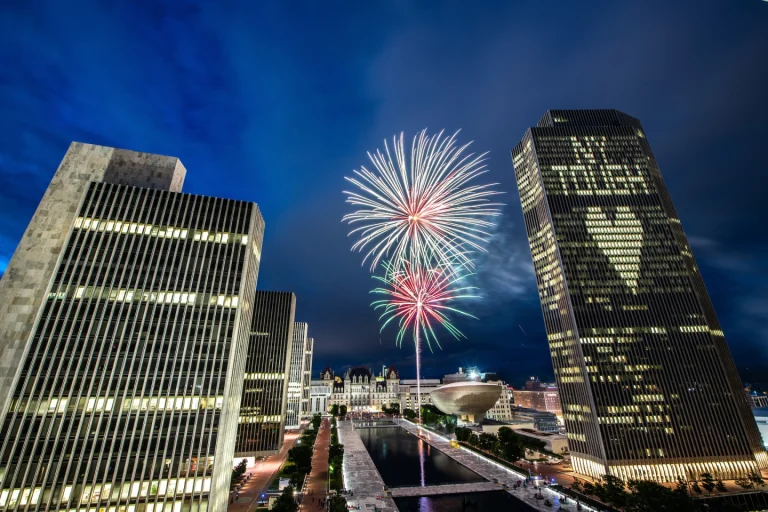 Kleurrijk vuurwerk explodeert in de lucht boven de wolkenkrabbers en het ronde gebouw van Empire State Plaza in Albany bij nacht