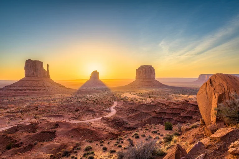 Opkomende zon tussen de karakteristieke rotsformaties van Monument Valley in Arizona met een kronkelende weg ervoor