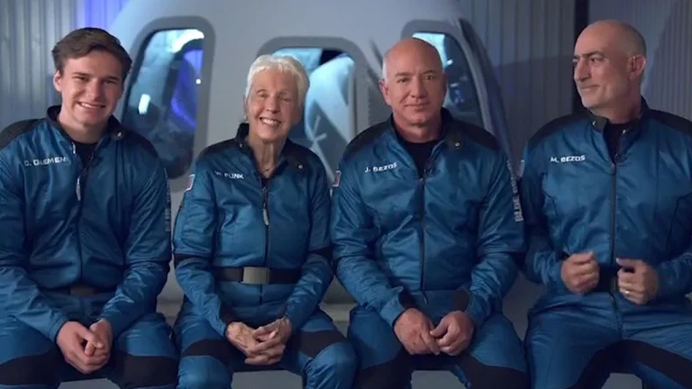 Vier bemanningsleden in blauwe vluchtpakken zitten poserend voor de camera voorafgaand aan hun vlucht met Blue Origin