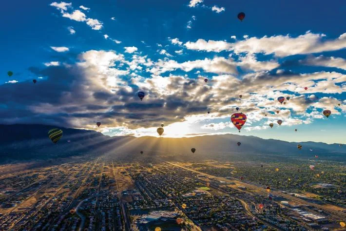 Groot aantal kleurrijke heteluchtballonnen zweeft in de ochtendlucht boven de stad Albuquerque met bergen op de achtergrond