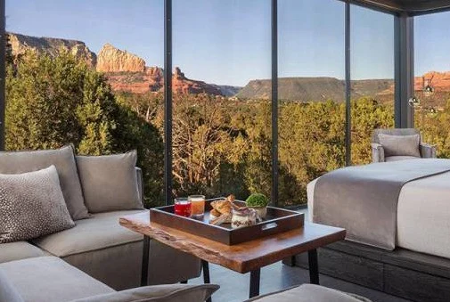 Moderne hotelkamer met grote raampartijen, een loungehoek en bed met uitzicht op de rode rotsformaties van Sedona