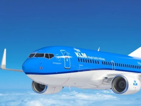 Blauw wit vliegtuig van KLM vliegt door een heldere blauwe lucht boven een wolkendek