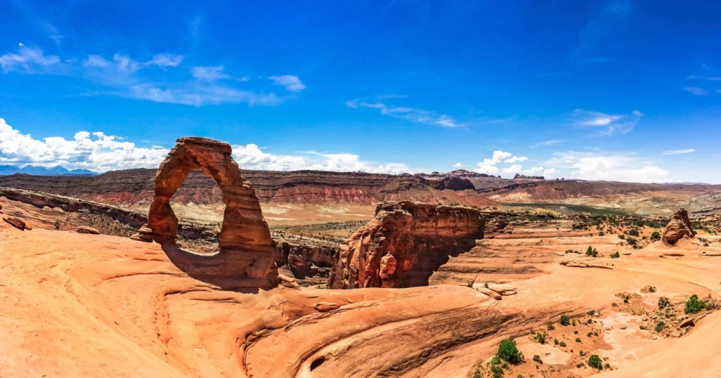 De vrijstaande zandstenen boog Delicate Arch torent boven een rotsplateau uit met wijds uitzicht op de vallei in Utah