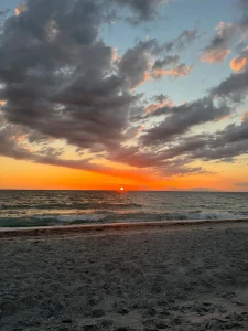 Oranje en roze gekleurde wolkenlucht boven de zee met golven die uitrollen op een leeg zandstrand bij zonsondergang