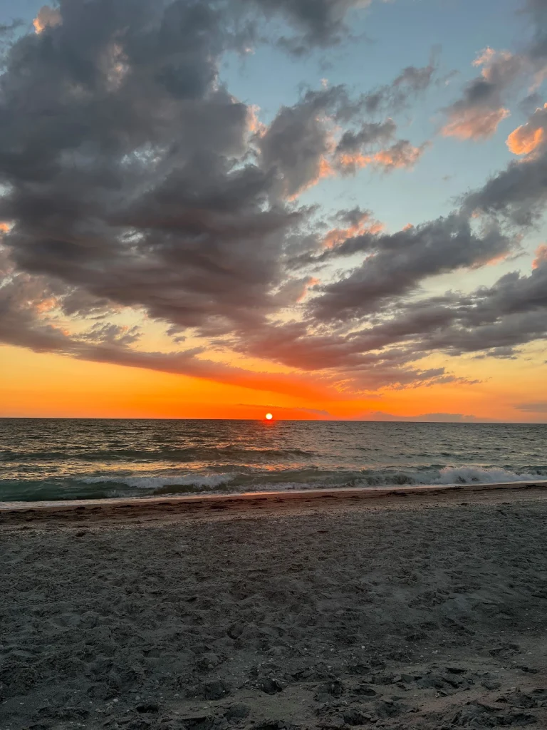 Oranje en roze gekleurde wolkenlucht boven de zee met golven die uitrollen op een leeg zandstrand bij zonsondergang