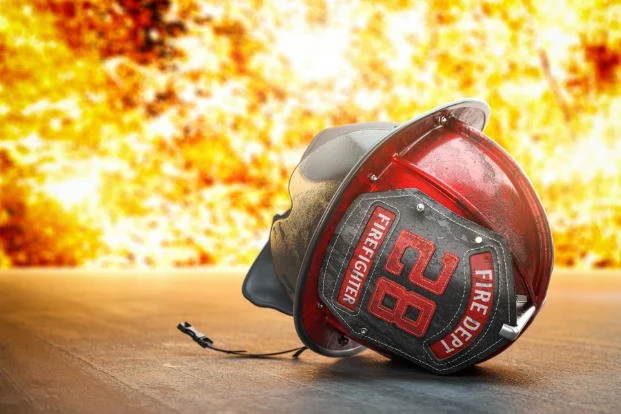 Gedeukte rood zwarte brandweerhelm met het nummer 28 ligt op de grond tegen een achtergrond van felle vlammen