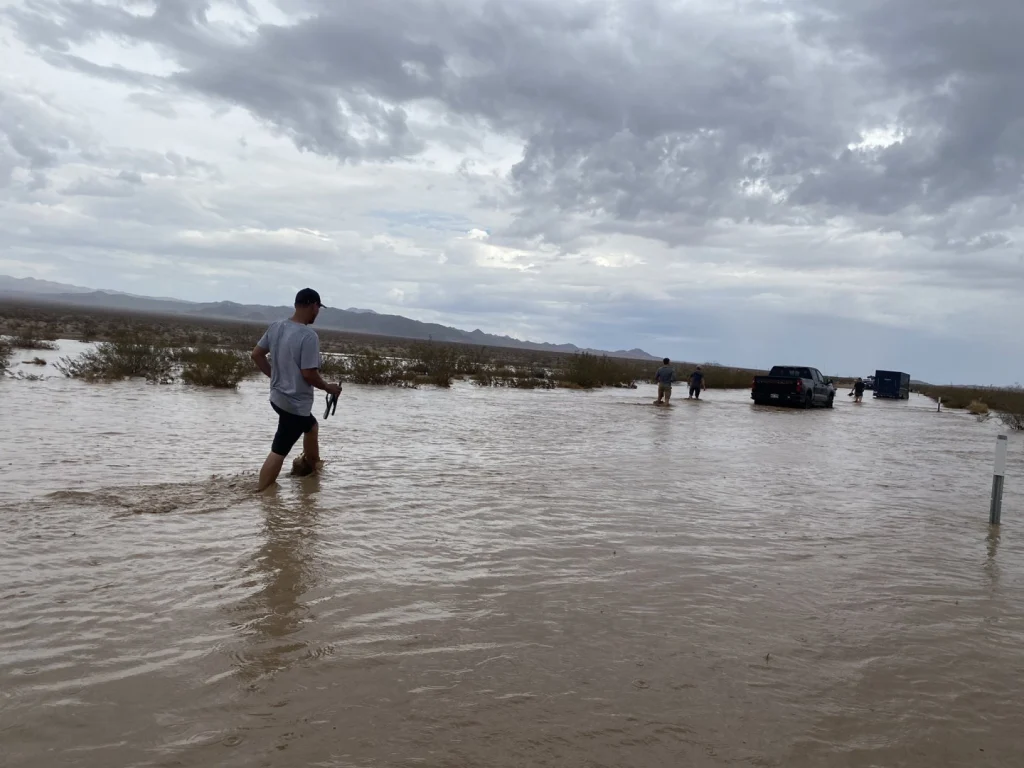 Mensen waden door bruin overstromingswater op een weg terwijl auto's vaststaan in de verte in Death Valley