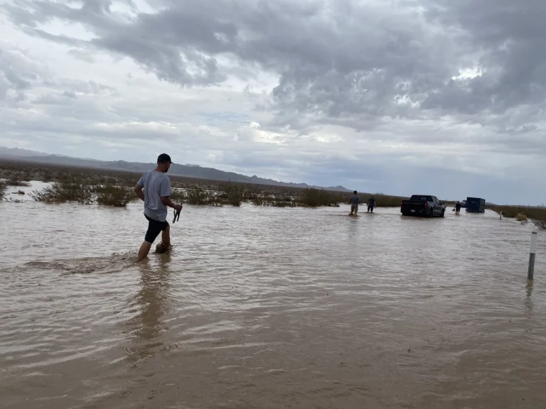 Mensen waden door bruin overstromingswater op een weg terwijl auto's vaststaan in de verte in Death Valley