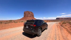 Zwarte terreinwagen staat op een rode zandweg met de rotsformatie Merrick Butte op de achtergrond in Monument Valley