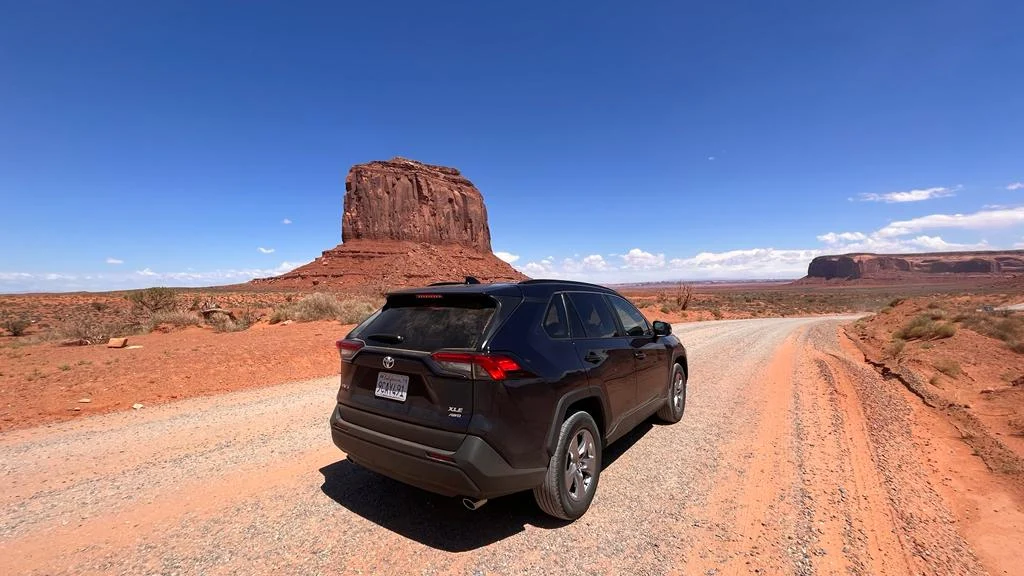 Zwarte terreinwagen staat op een rode zandweg met de rotsformatie Merrick Butte op de achtergrond in Monument Valley