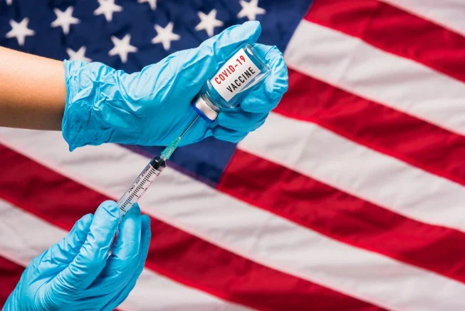 Handen in blauwe handschoenen vullen een injectiespuit met vaccin uit een flesje voor een Amerikaanse vlag