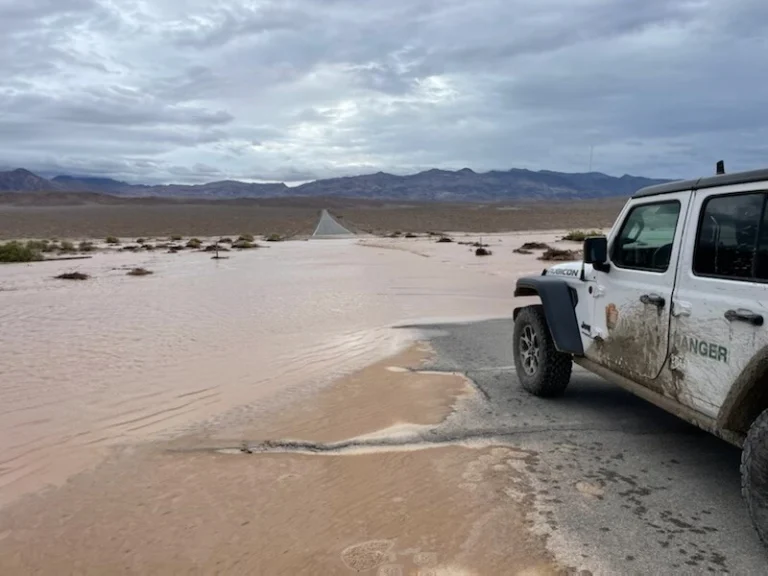 Witte terreinwagen van een parkranger staat naast een door overstromingswater bedekte weg in het uitgestrekte landschap van Death Valley