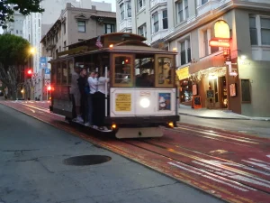 Klassieke houten kabeltram met passagiers rijdt bij schemering door een helling in San Francisco langs verlichte gevels