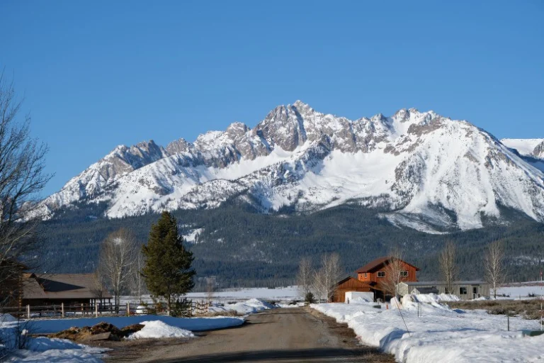 Hoge besneeuwde bergketen van de Sawtooth Mountains achter een besneeuwd landweggetje met een houten schuur in Stanley, Idaho