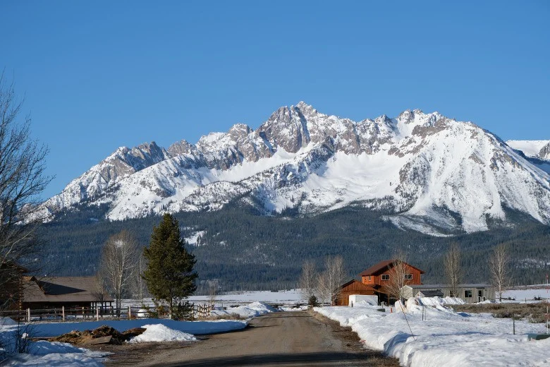 Hoge besneeuwde bergketen van de Sawtooth Mountains achter een besneeuwd landweggetje met een houten schuur in Stanley, Idaho