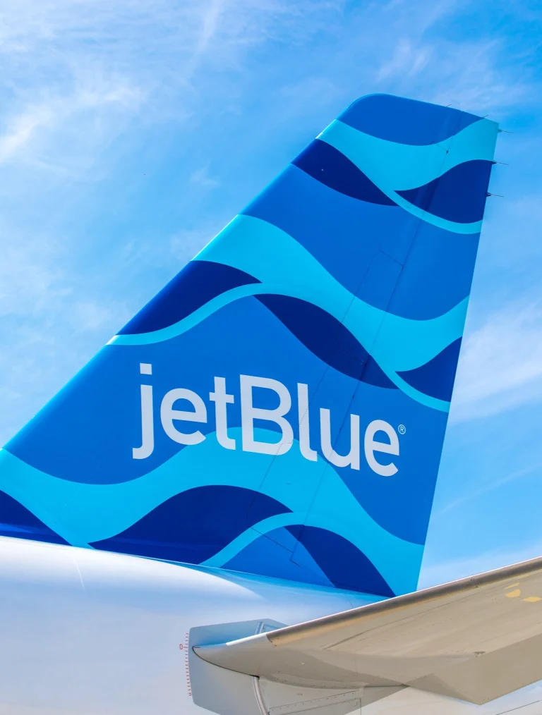 Close-up van de blauwe staartvin van een JetBlue toestel met een golvend patroon en het logo, gefotografeerd vanuit een ander vliegtuig