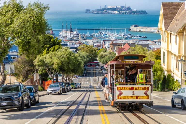 Rood bruine kabeltram rijdt een steile straat af met op de achtergrond de jachthaven en het eiland Alcatraz in San Francisco