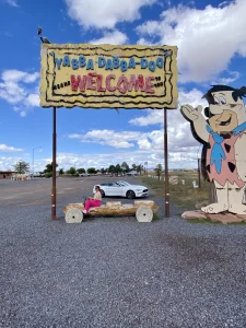 Bord met de tekst Yabba Dabba Doo Welcome naast een levensgrote figuur van Fred Flintstone en een witte cabriolet