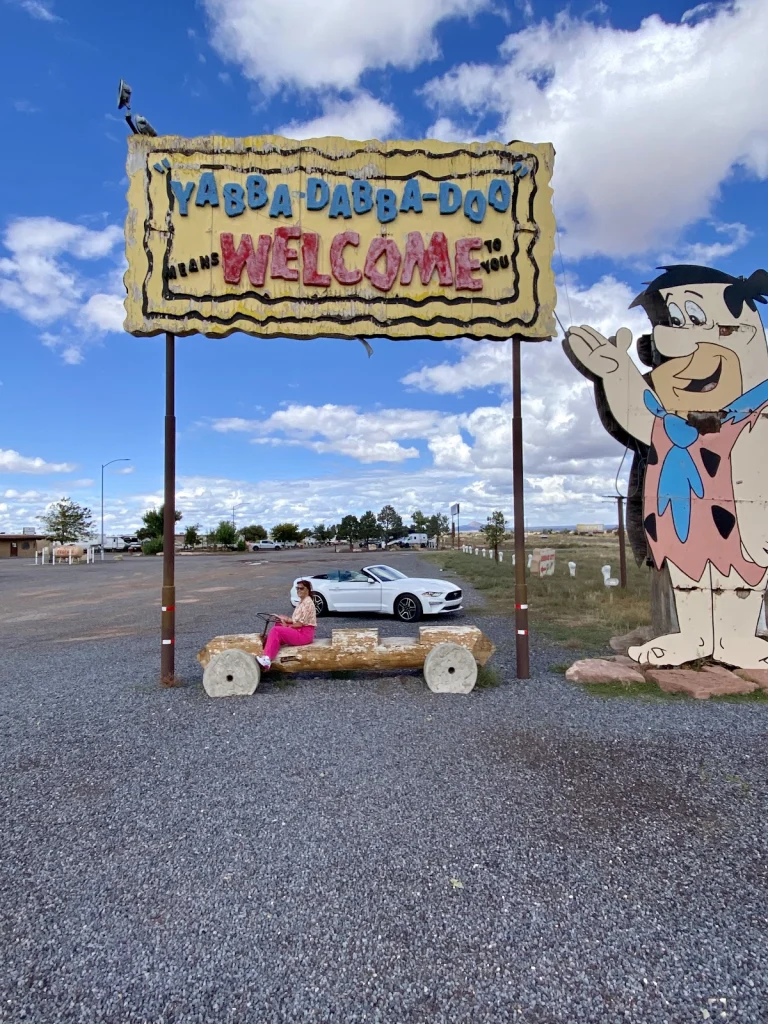 Bord met de tekst Yabba Dabba Doo Welcome naast een levensgrote figuur van Fred Flintstone en een witte cabriolet