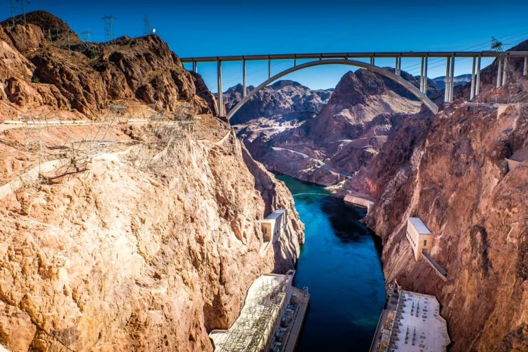 Uitzicht op de gebogen brug die over de diepe kloof van de Colorado River spant, met de Hoover Dam en rotsachtige bergen op de achtergrond
