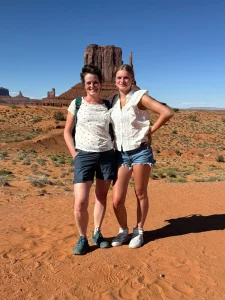 Twee vrouwen staan naast elkaar op het rode zand van Monument Valley met een hoge rotstoren op de achtergrond
