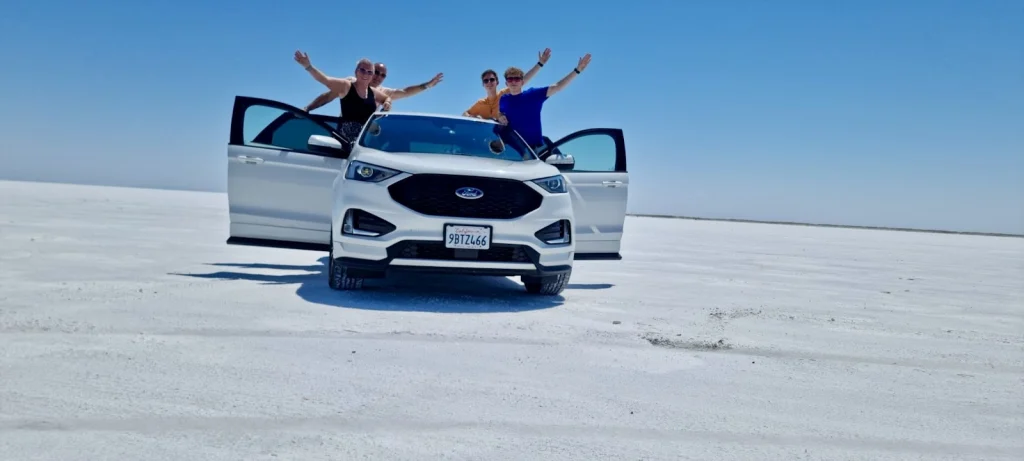 Drie mensen zwaaien vanaf een witte suv die midden op de witte zoutvlakte van de Bonneville Salt Flats staat