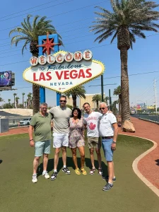 Vijf mensen staan lachend voor het beroemde Welcome to Fabulous Las Vegas bord tussen palmbomen