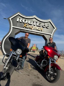 Twee mannen poseren met hun motorfietsen onder het grote Route 66 bord van Kingman in Arizona
