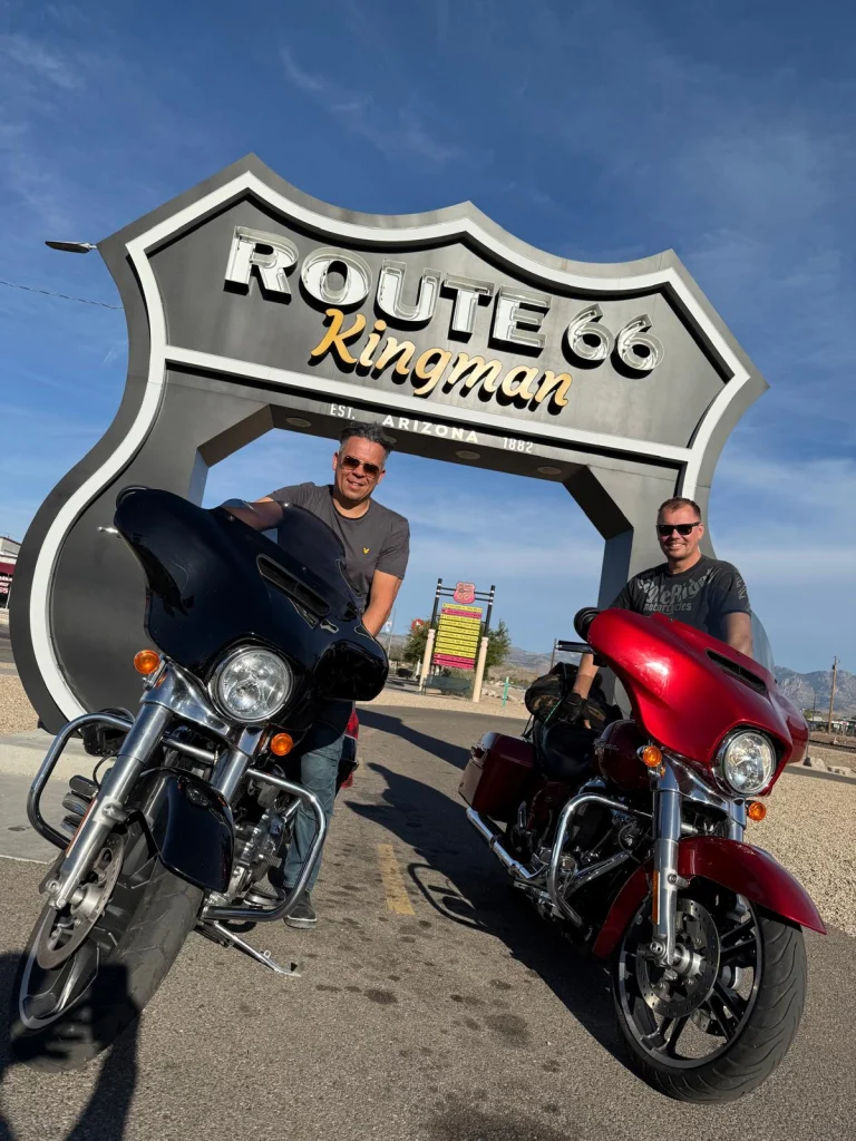 Twee mannen poseren met hun motorfietsen onder het grote Route 66 bord van Kingman in Arizona