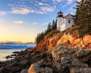 Witte vuurtoren met rood dak op een rotsachtige, oranje gekleurde kust met dennenbomen in Acadia National Park in Maine