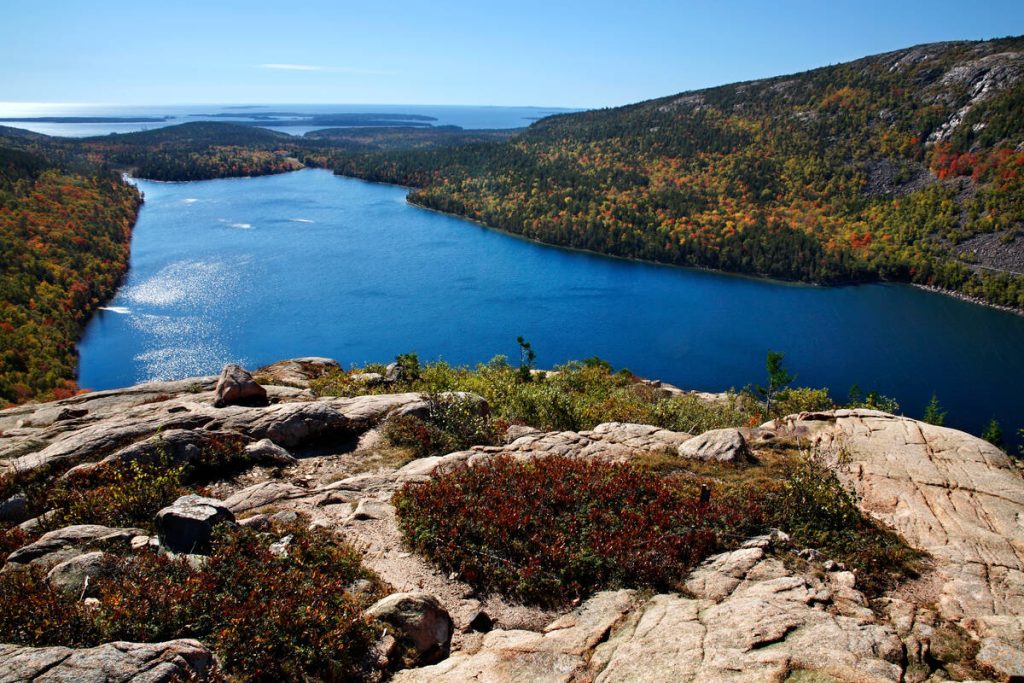 Uitzicht vanaf een rotsachtige bergtop over het blauwe water van Jordan Pond in Acadia National Park, omringd door herfstkleurig bos