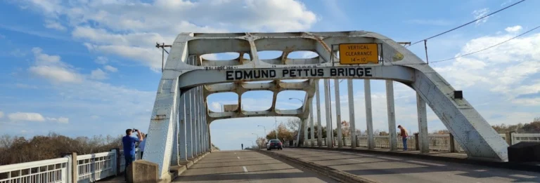 De stalen boogbrug Edmund Pettus Bridge in Selma, Alabama, met wandelaars op de weg onder een blauwe lucht