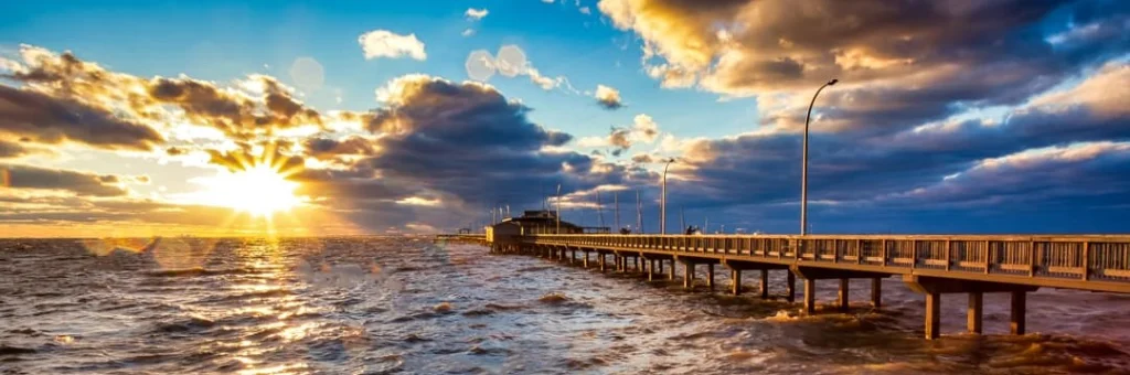 Lange houten pier steekt de golvende zee in terwijl de zon opkomt boven de horizon aan de Alabama golfkust