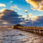 Lange houten pier steekt de golvende zee in terwijl de zon opkomt boven de horizon aan de Alabama golfkust
