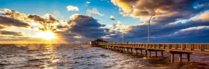 Lange houten pier steekt de golvende zee in terwijl de zon opkomt boven de horizon aan de Alabama golfkust