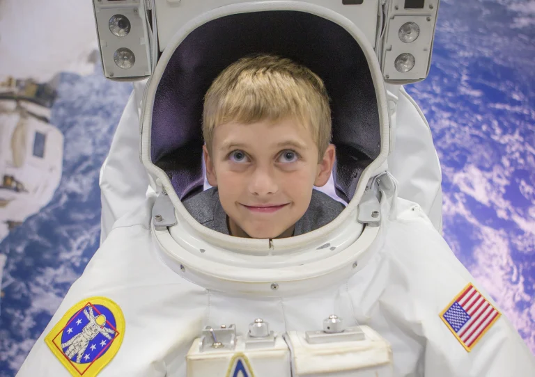 Een lachende jongen steekt zijn hoofd door een astronautenpak met Amerikaanse vlag in het US Space & Rocket Center in Huntsville, Alabama