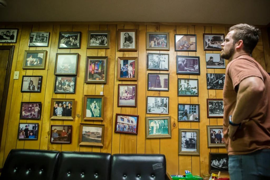 Man bekijkt een houten wand vol ingelijste foto's van muzikanten in de FAME Studios in Muscle Shoals, Alabama