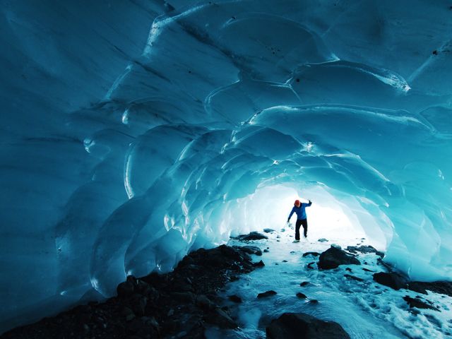Een persoon in rode muts loopt door een indrukwekkende blauwe ijsgrot op een gletsjer in Alaska